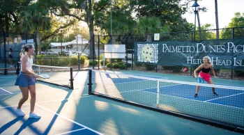 two girls playing pickleball with the sun shining through the trees