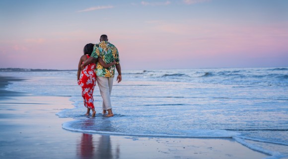 couple in floral clothing embracing each other as they walk along the water with the sunset on the beach