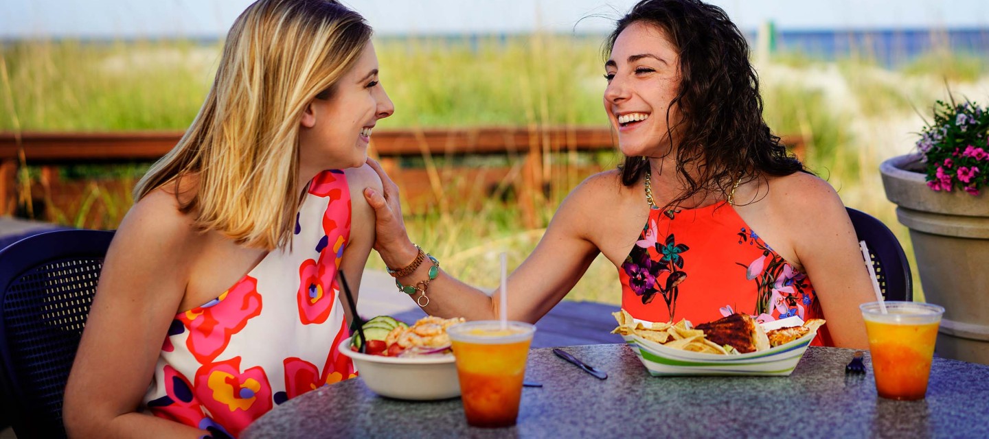 two young woman enjoying laughs among dinner and drinks at Dunes House outdoor dining