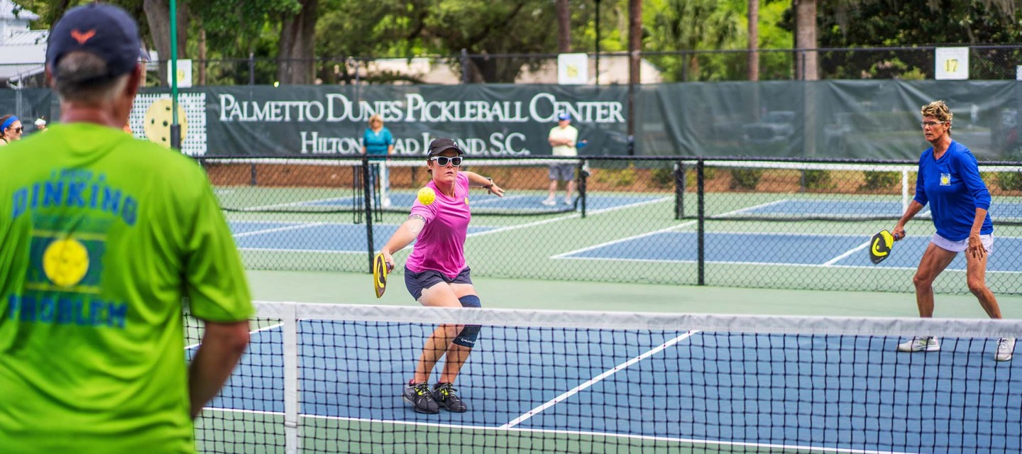 three pickleball players actively playing a game on Palmetto Dunes Pickleball court