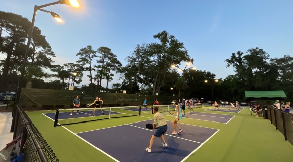 group of pickleball players playing on several courts under the evening sky and lights