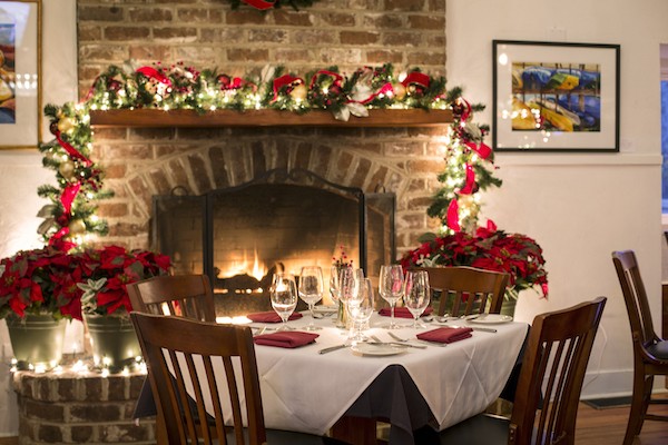 Table setting in front of the fireplace decorated with Christmas garland and poinsettias at Alexander's Restaurant and Wine Bar