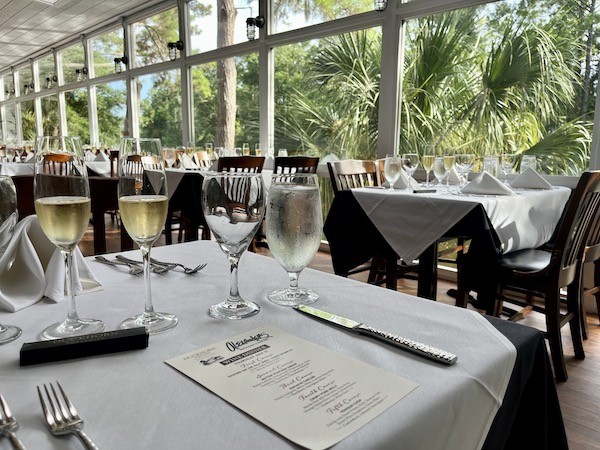 wine dinner table setting with wine glasses and drinking glasses on white tablecloths with large windows at Alexander's