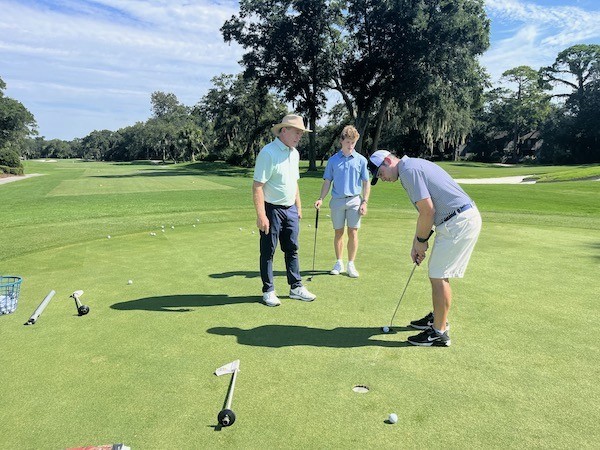 man practicing his putt on the golf course with Doug Weaver and son watching