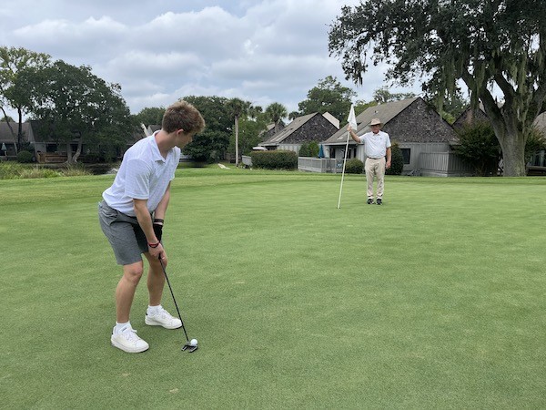 son puts his ball into the whole with Doug Weaver holding the flag