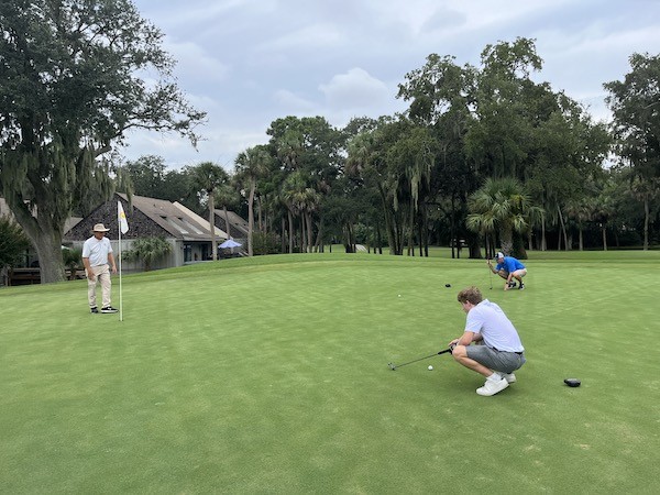 two men squatting over golf ball looking at hole with Doug Weaver