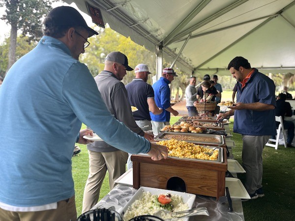 male golfers grabbing food at the buffet under the tent