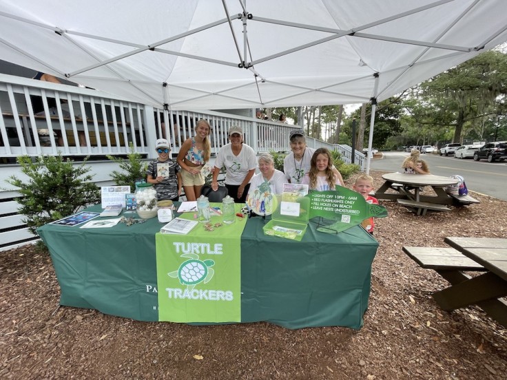 group of volunteers and visitors at the Turtle Trackers booth outside of the Palmetto Dunes General Store
