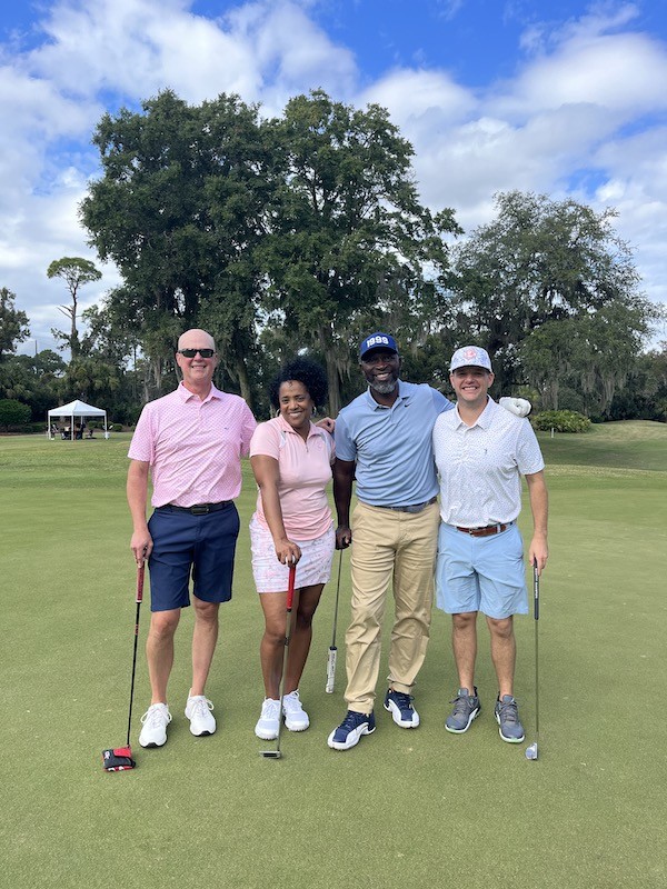 group of four golfers smiling on the green