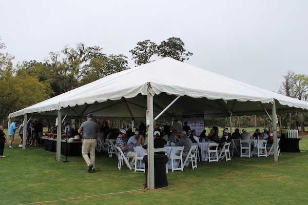 group gathering at round tables under a tent on the golf course