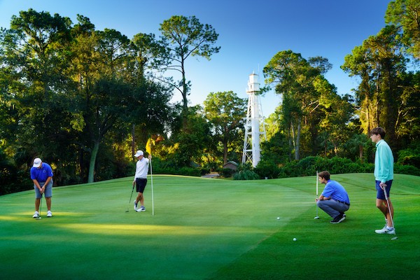 golfers watching another golfer putting on the Arthur Hills Golf Course with the lighthouse in the background