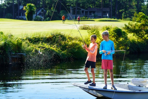 two boys fishing on the edge of a boat in the Palmetto Dunes Lagoon