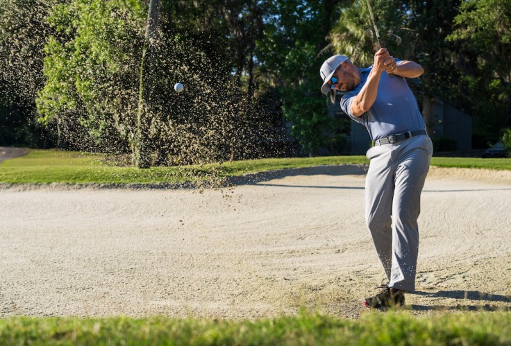 golfer swinging with sand in the air in a golf sand pit