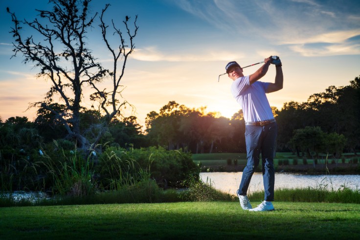 golfer swinging with water and sunsetting behind him