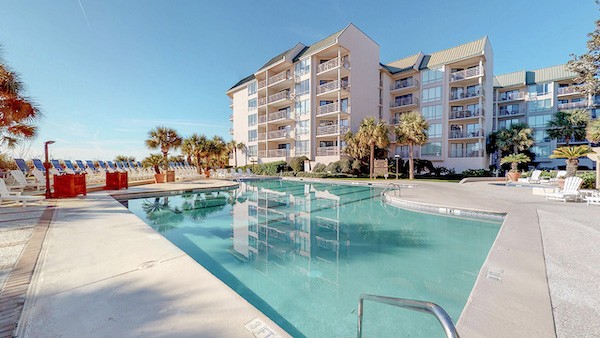 view of pool with dunes and condos in the background at the Villamare Complex