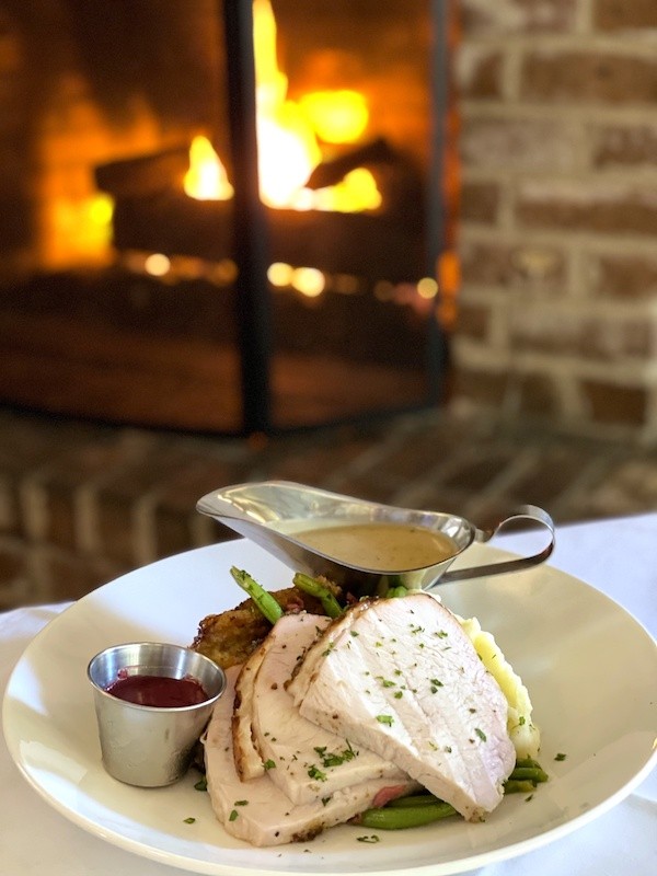 sliced turkey breast with gravy and cranberry sauce with fire in the background