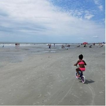 little girl in swimsuit biking on beach
