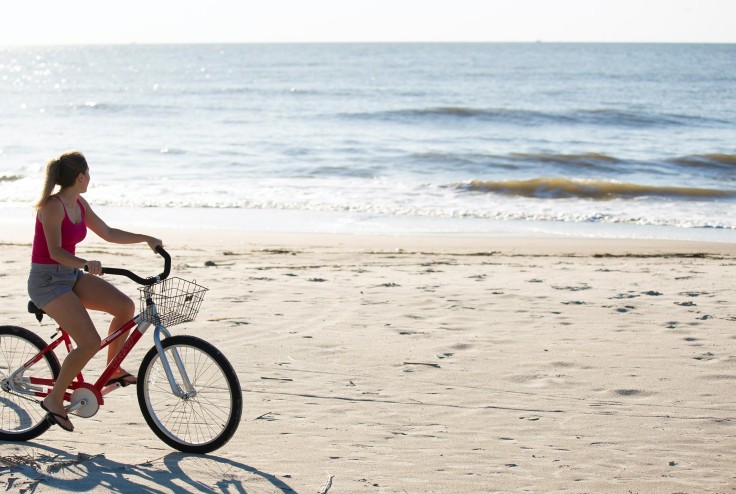 woman on red bike biking on the beach looking out over the waves