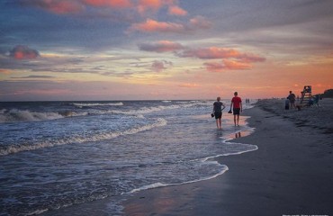 couple walking the shallow ocean water with pink and blue sunset in the background