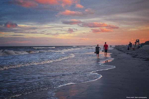 couple walking the shallow ocean water with pink and blue sunset in the background