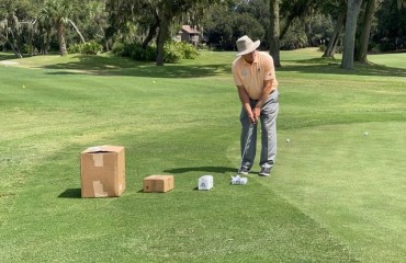 palmetto dunes golf instructor doug weaver in peach shirt and white hat putting in front of four boxes