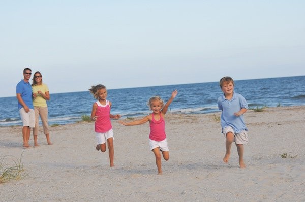 three kids running on beach while parents watch in the back