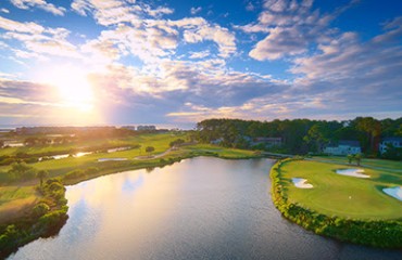 sun flare and blue skies over the water and greens of Robert Trent Jones Golf Course