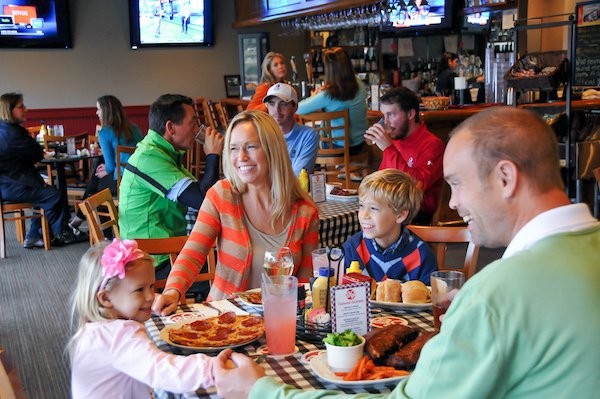 Family dining and laughing at Big Jim's with sports on TVs above the bar