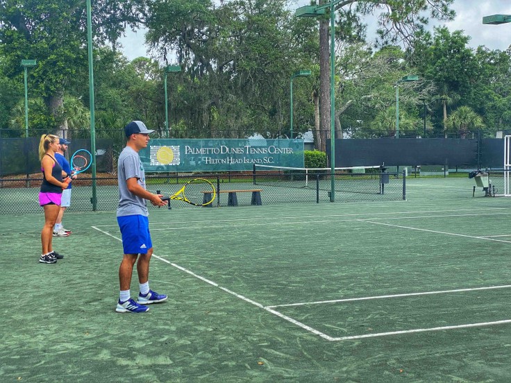 tennis students on the tennis court listening to instructor holding rackets