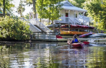 woman in red kayak on water in front of hilton head outfitters dock