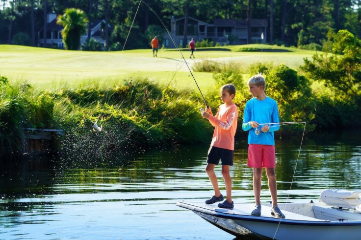 two boys standing on boat fishing in palmetto dunes lagoon along golf course