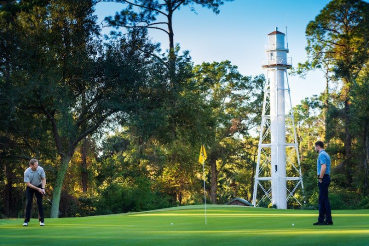 two golfers putting in front of lighthouse