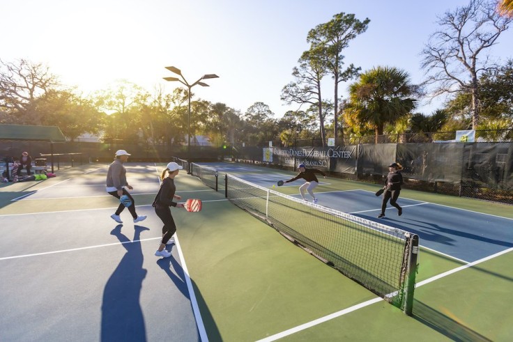four pickleball players in action with sun setting in the background behind trees