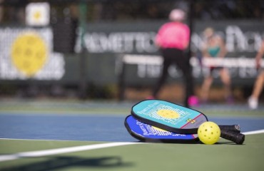 pickleball paddles and ball on court with players blurred in the background