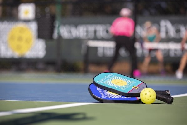 pickleball paddles and ball on court with players blurred in the background