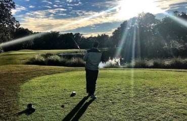 Golfer after his swing on the course with sun glare in the sky