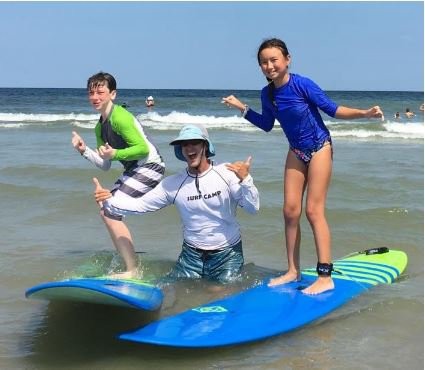 girl and boy on surf boards in ocean with surf instructor