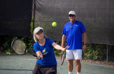 woman practicing her serve with tennis pro instructor observing in the background