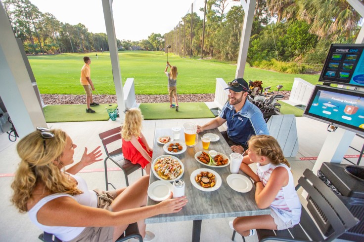 family laughing and eating with children swinging at the range at Toptracer Driving Range