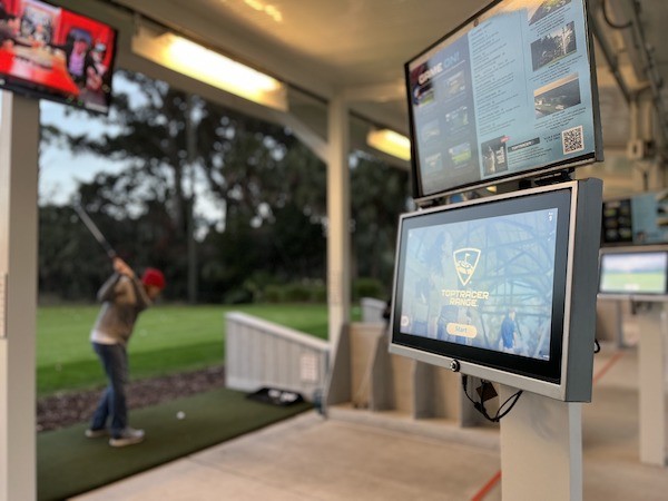 up close view of the Toptracer driving range screen with a woman swinging in the background