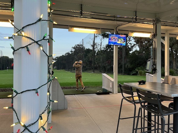 golfer post swing at the driving range with Christmas lights wrapped around the pole in the foreground