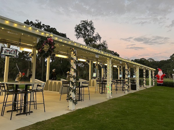 view of the driving range with lights along the roof and poles with the sunset in the background