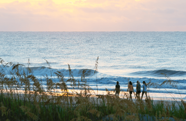 family walking along the beach with waves and pink sunrise in background