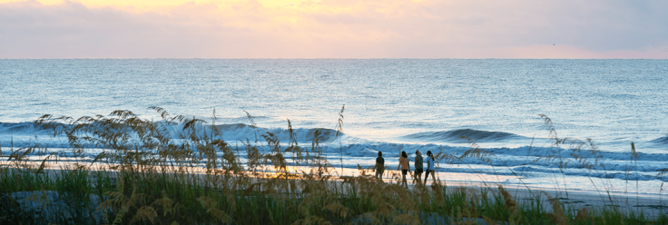 family walking along the beach with waves and pink sunrise in background