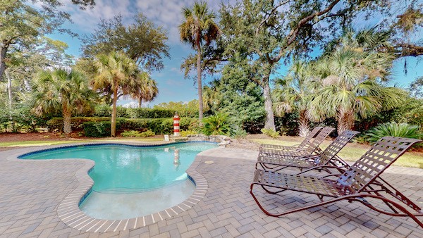 private pool with lounge chairs surrounded by trees in the backyard of a Hilton Head Island vacation home