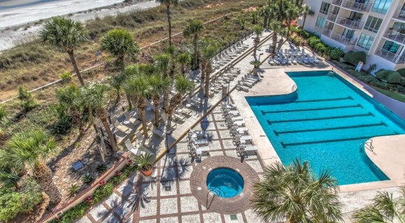 aerial view of large community pool with plenty of seating overlooking the dunes and ocean