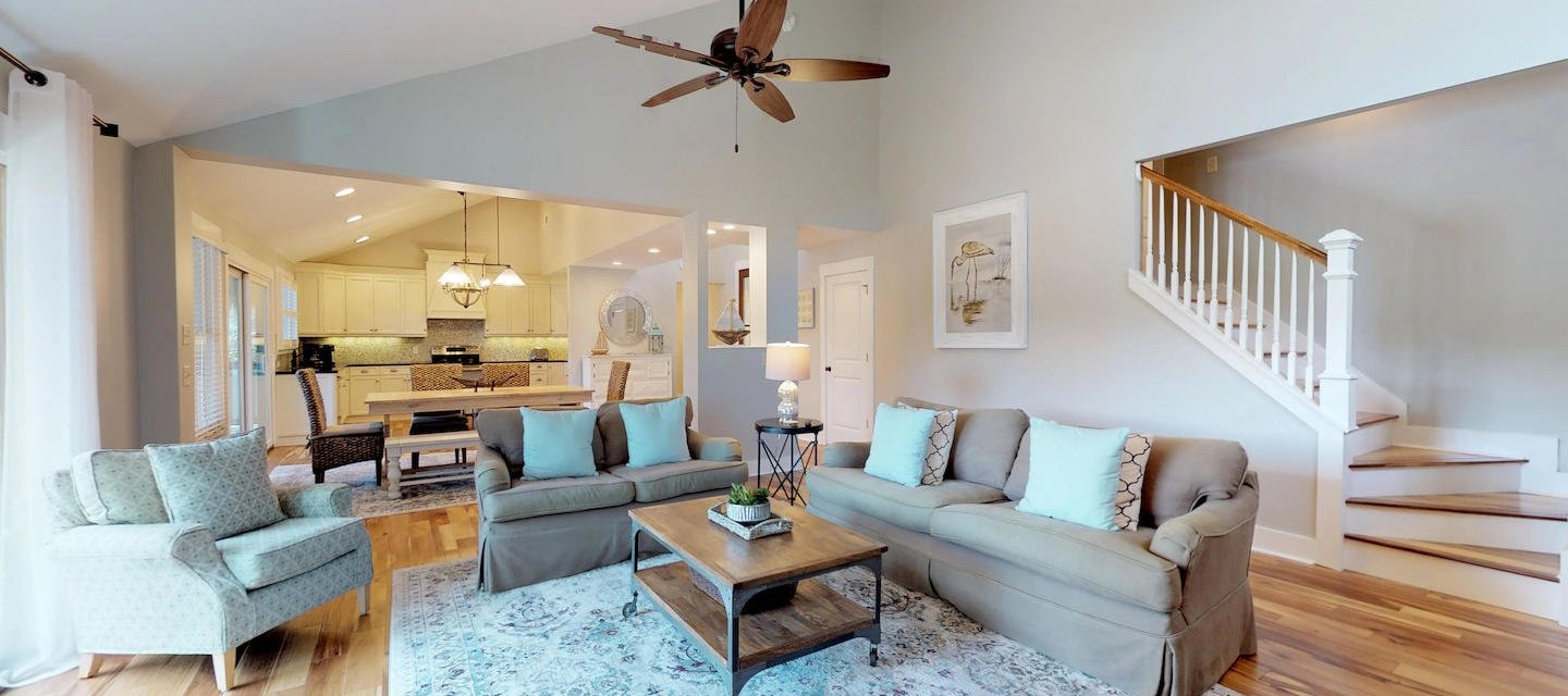 open plan living area of rental home with tan and blue couches and white kitchen in the background