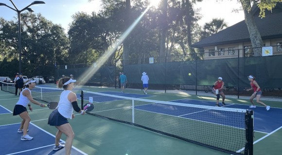 group of pickleball players actively playing a game at Palmetto Dunes Pickleball center with the sun shining through the trees