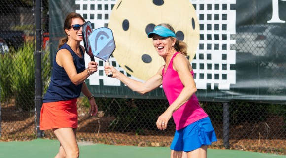 two women pickleball players smiling and tapping paddles at Palmetto Dunes Pickleball Center