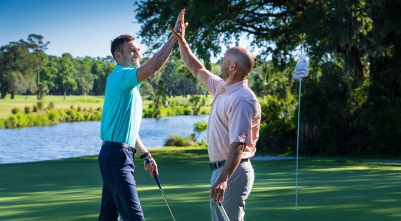 two golfers giving each other a high five on the course with water and flag in the background